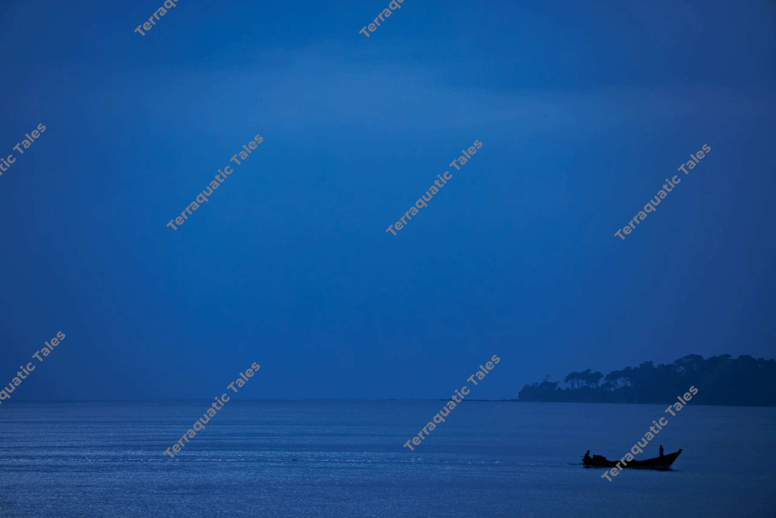 A small boat silhouetted on calm blue ocean waters off the coast of the Andaman Islands at dusk.