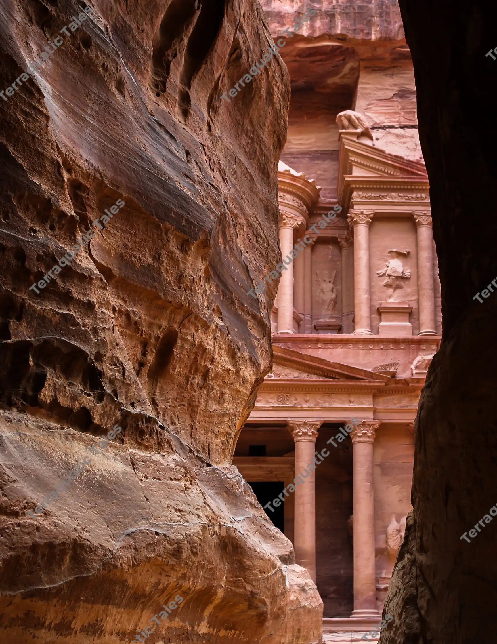 A vertical composition framing the rose-red carved facade of The Treasury (Al-Khazneh) as seen through the narrow, dark sandstone canyon walls of The Siq in Petra, Jordan.